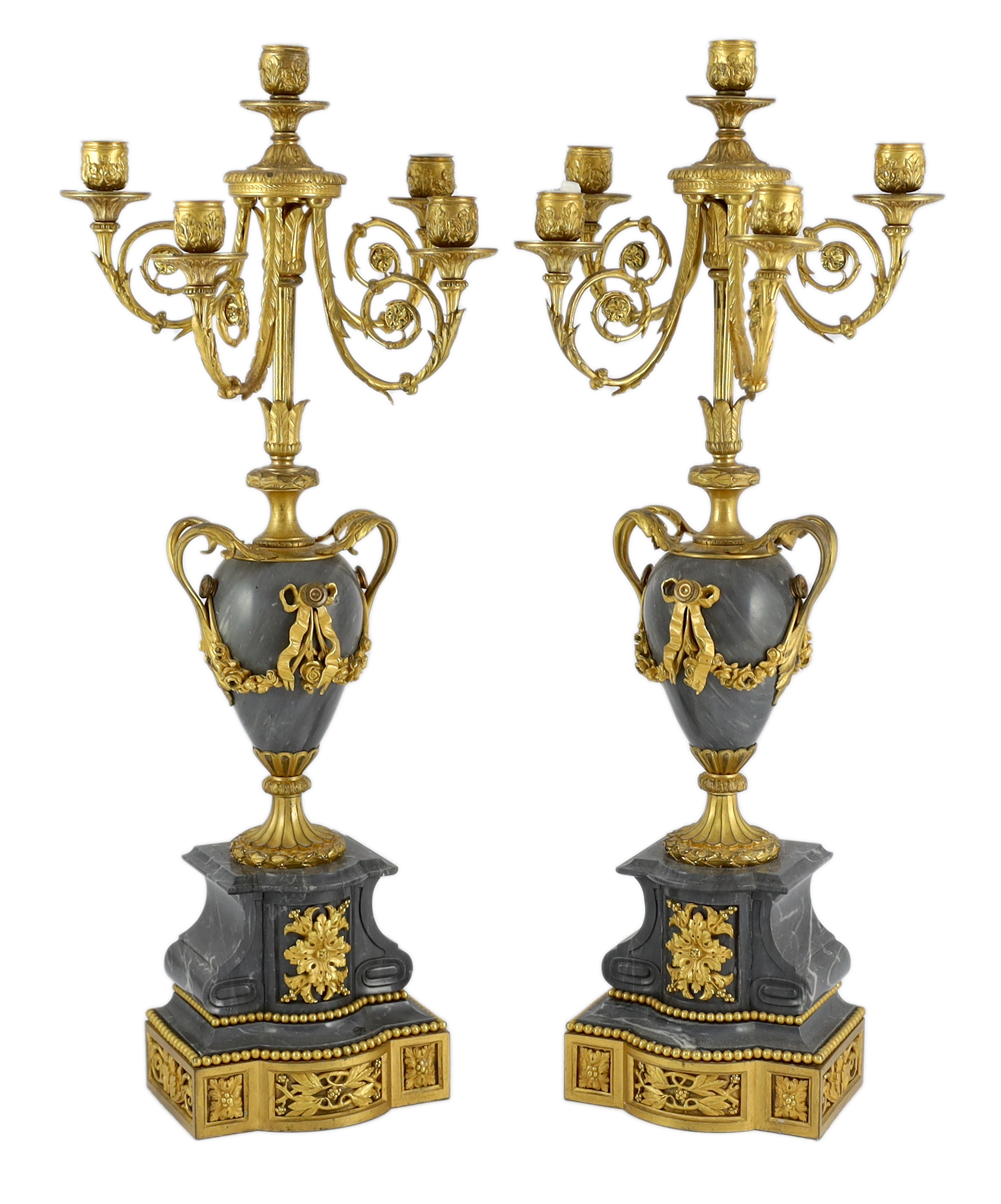A pair of Louis XVI style ormolu and grey marble five light candelabra, with scrolling branches and urn shaped stems on architectural plinths, 26cm wide, 63cm high